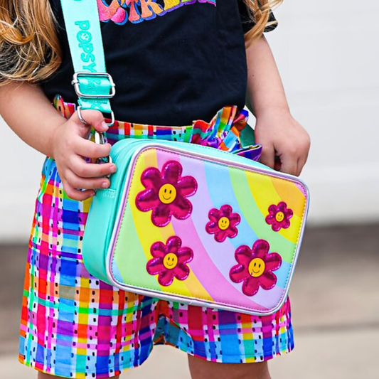 A close up of a girl wearing a green kids crossbody bag with a colourful flower interchangeable cover.