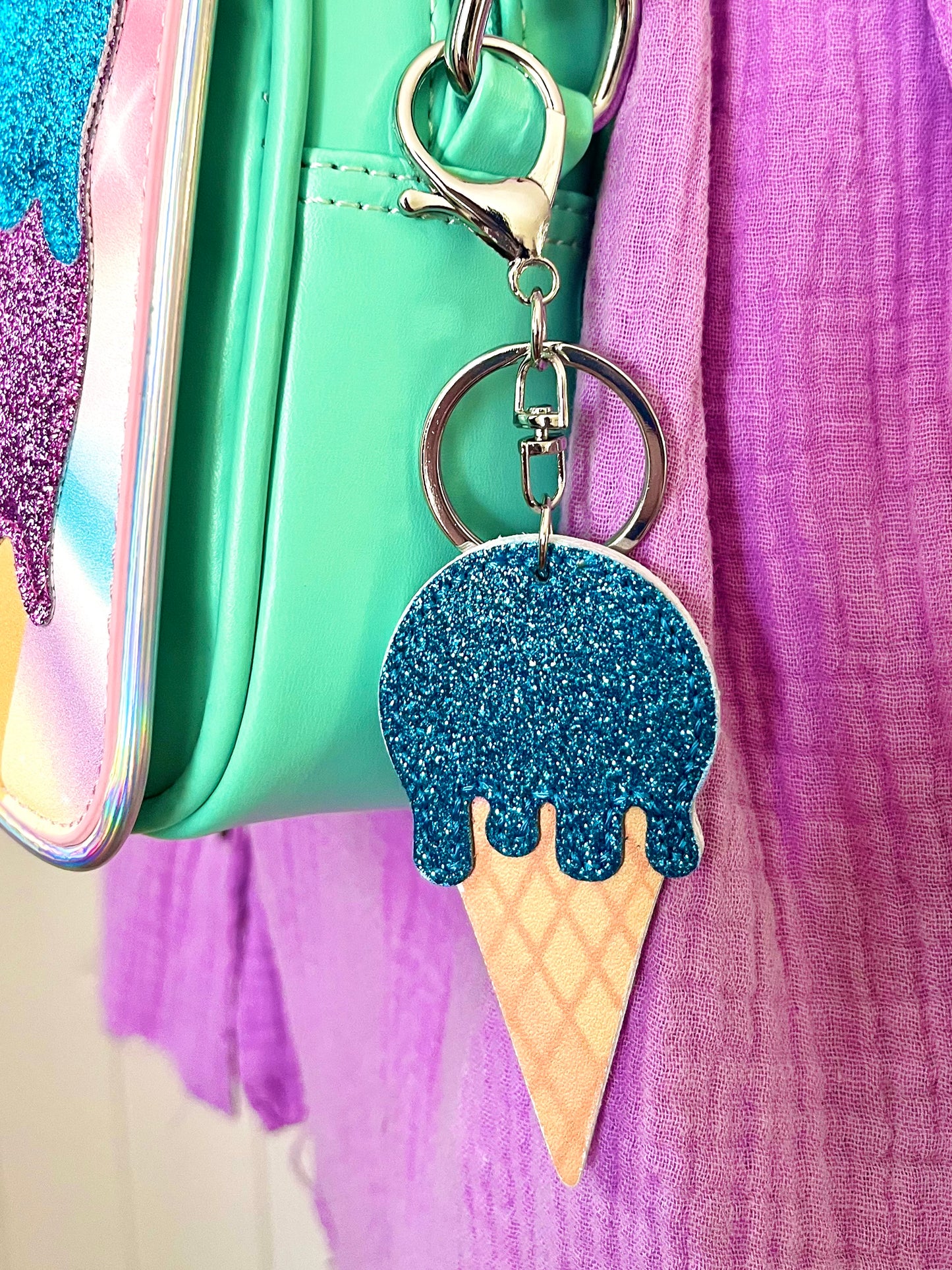 Blue glitter icecream bag charm. It is clipped onto a Popsy & Co crossbody bag with a silver-like clip.