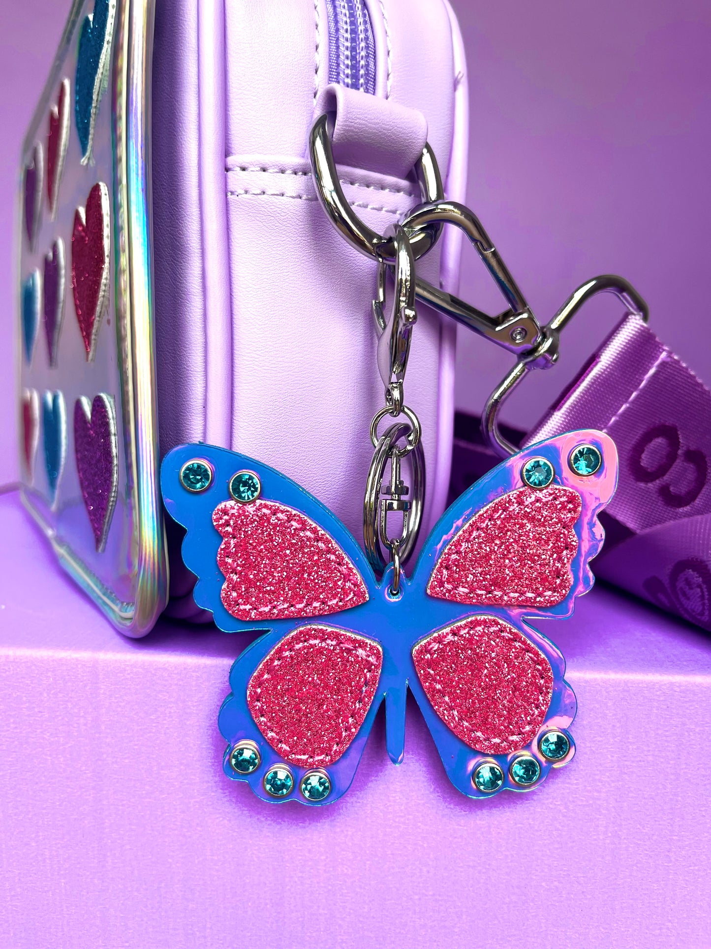 Glitter butterfly bag charm clipped to a Popsy and Co crossbody bag.