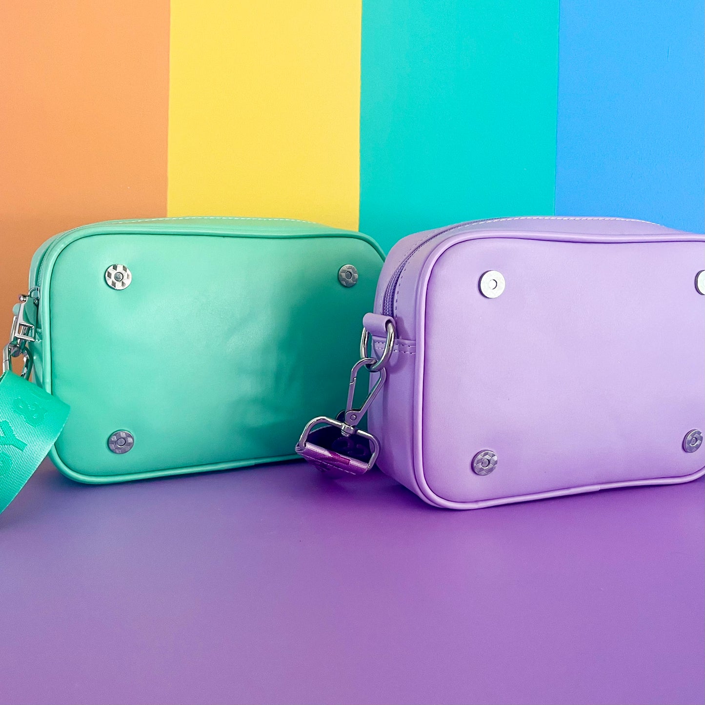 Kids crossbody bags from Popsy and Co. One is mint and the other is purple. They have magnetic clips on the front to attach a Popsy interchangeable cover. Includes an adjustable strap with branding on it.