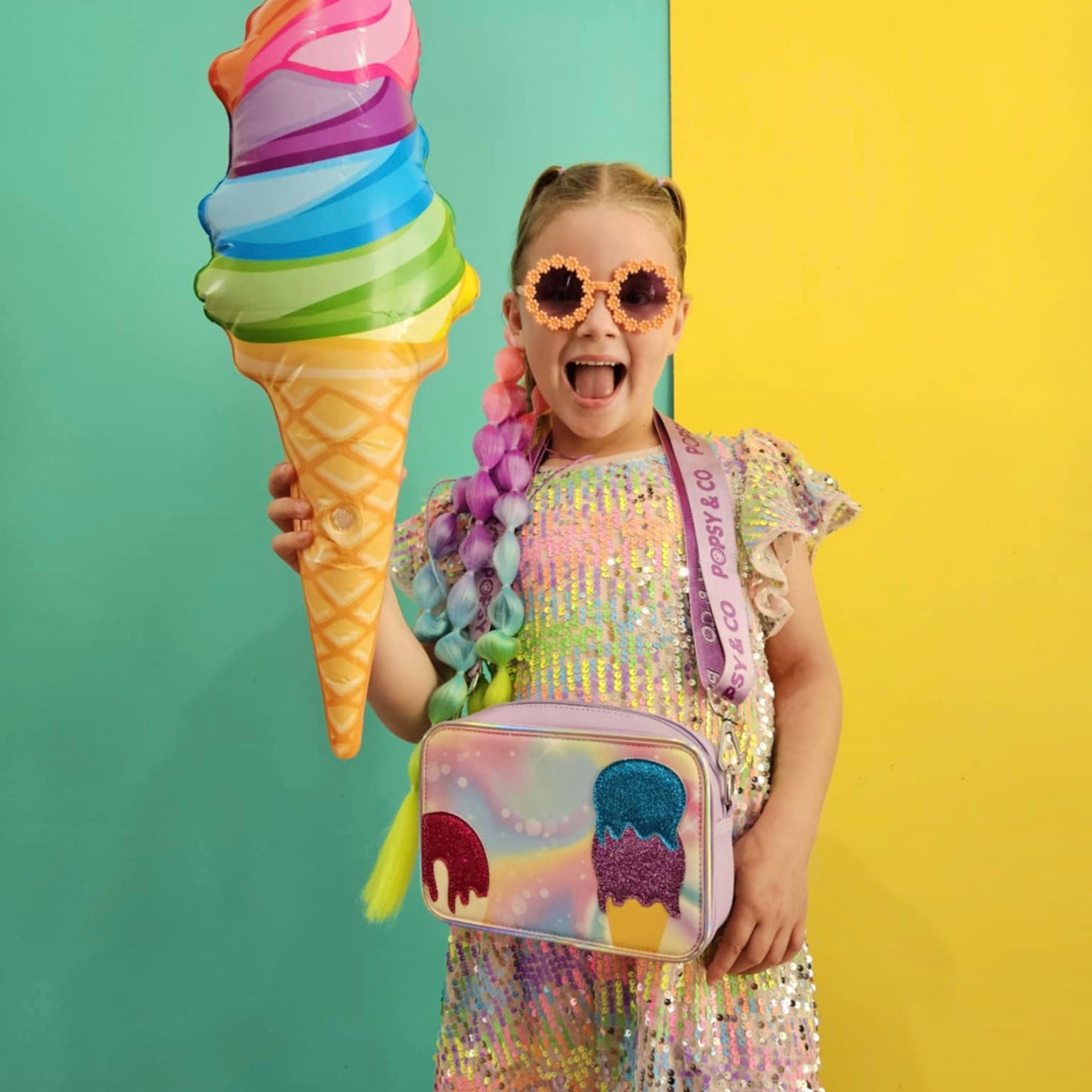Girl wearing sequin dress holding a purple kids crossbody bag with glittery ice-cream cover and balloon