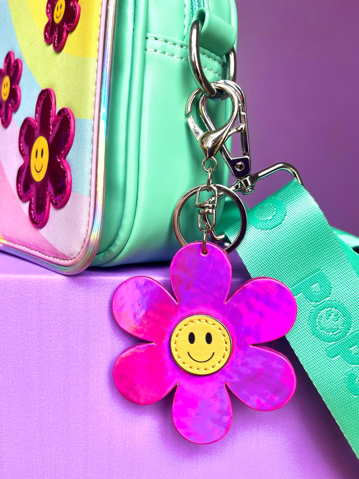 Pink flower bag charm with a yellow smiley in the middle. It is clipped onto a Popsy & Co crossbody bag.