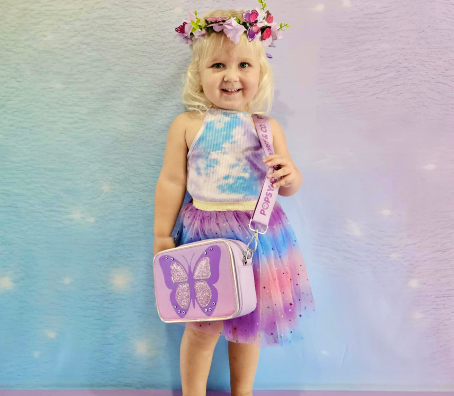 Girl wearing a kids purple crossbody bag with the butterfly wishes interchangeable cover from Popsy and Co.