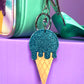 Icecream keychain with a blue glitter scoop on top of a cone. It is clipped onto a Popsy and Co bag.