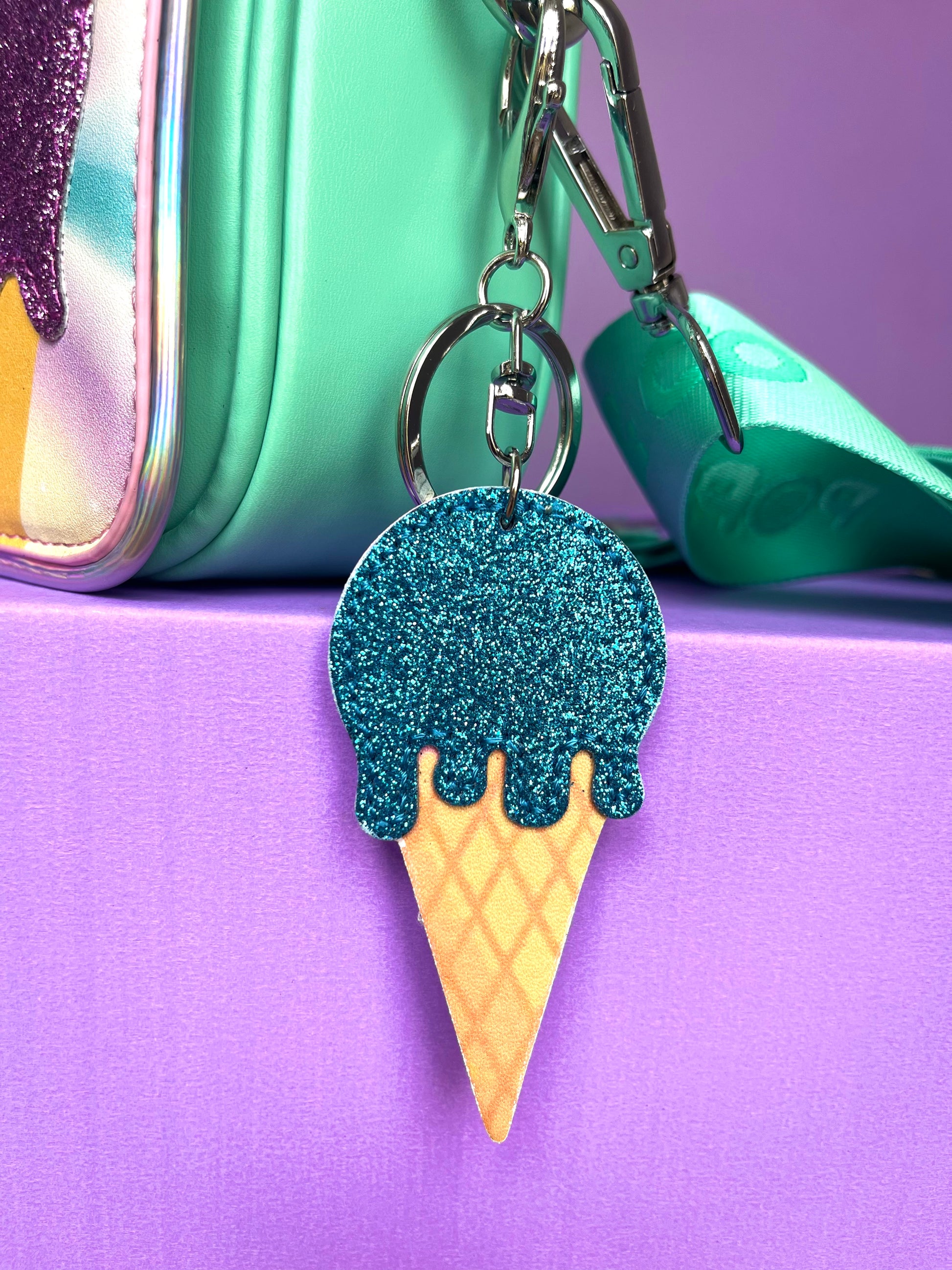 Icecream keychain with a blue glitter scoop on top of a cone. It is clipped onto a Popsy and Co bag.