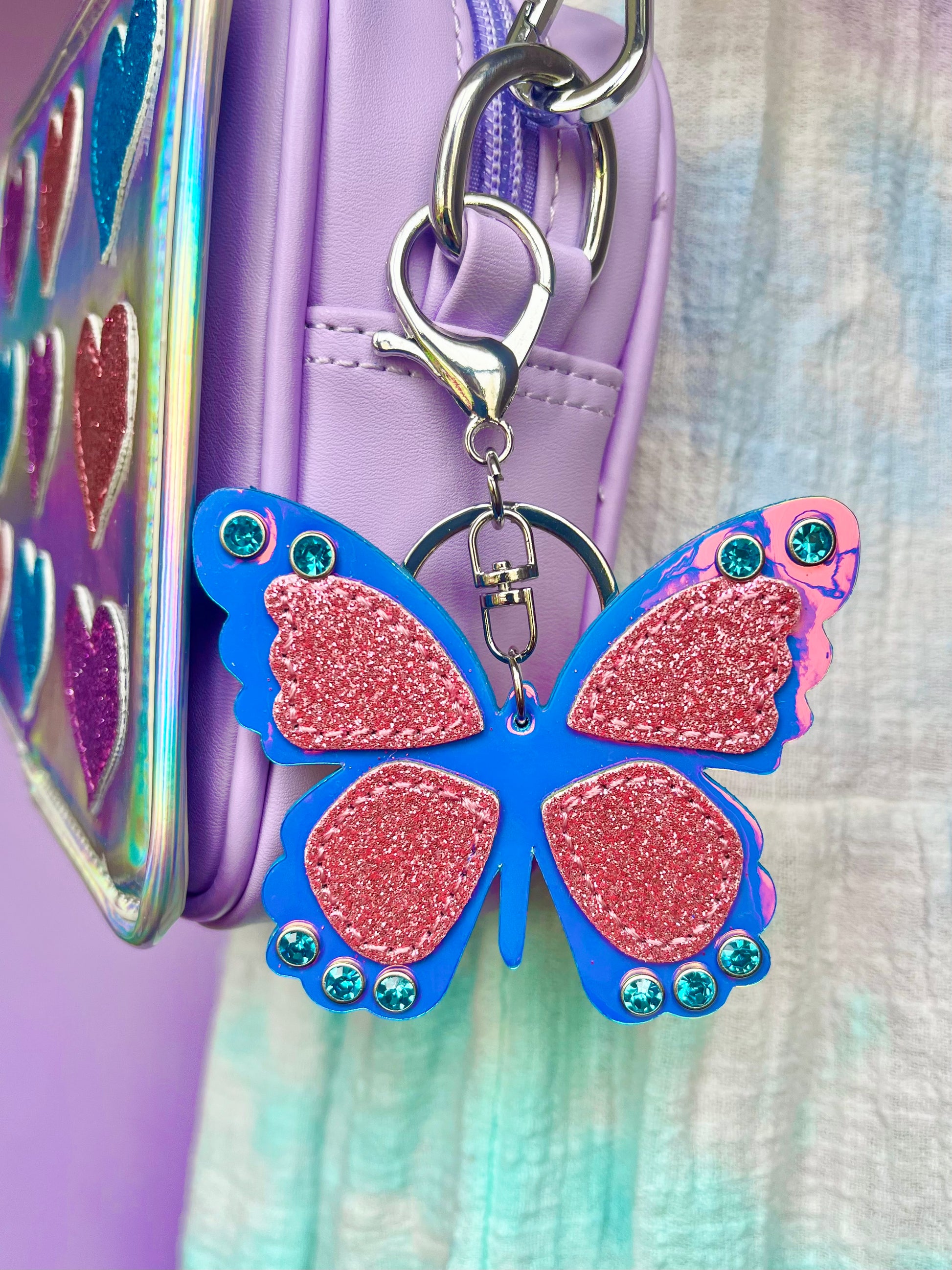 Butterfly keychain for kids. It has a purple metallic butterfly with pink glitter patches and blue gems.