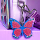 Glitter butterfly bag charm clipped to a Popsy and Co crossbody bag.