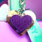 Glitter heart keychain for kids. Purple glitter heart on a silver metallic background. It is clipped to a Popsy and Co bag with a silver-like clip.