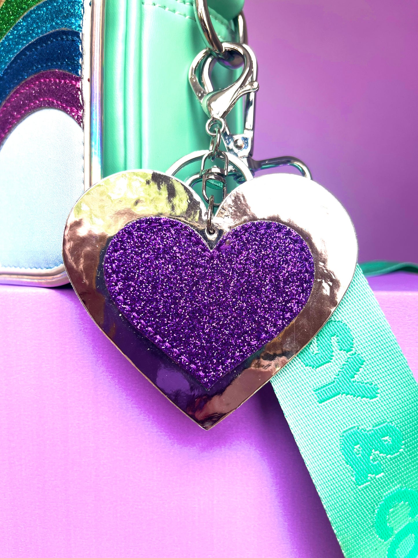 Glitter heart keychain for kids. Purple glitter heart on a silver metallic background. It is clipped to a Popsy and Co bag with a silver-like clip.