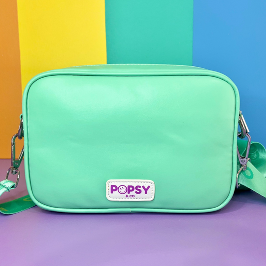 Mint coloured kids crossbody bag. Has magnetic clips on front to attach a Popsy interchangeable cover and logo on the back. Has an adjustable strap.
