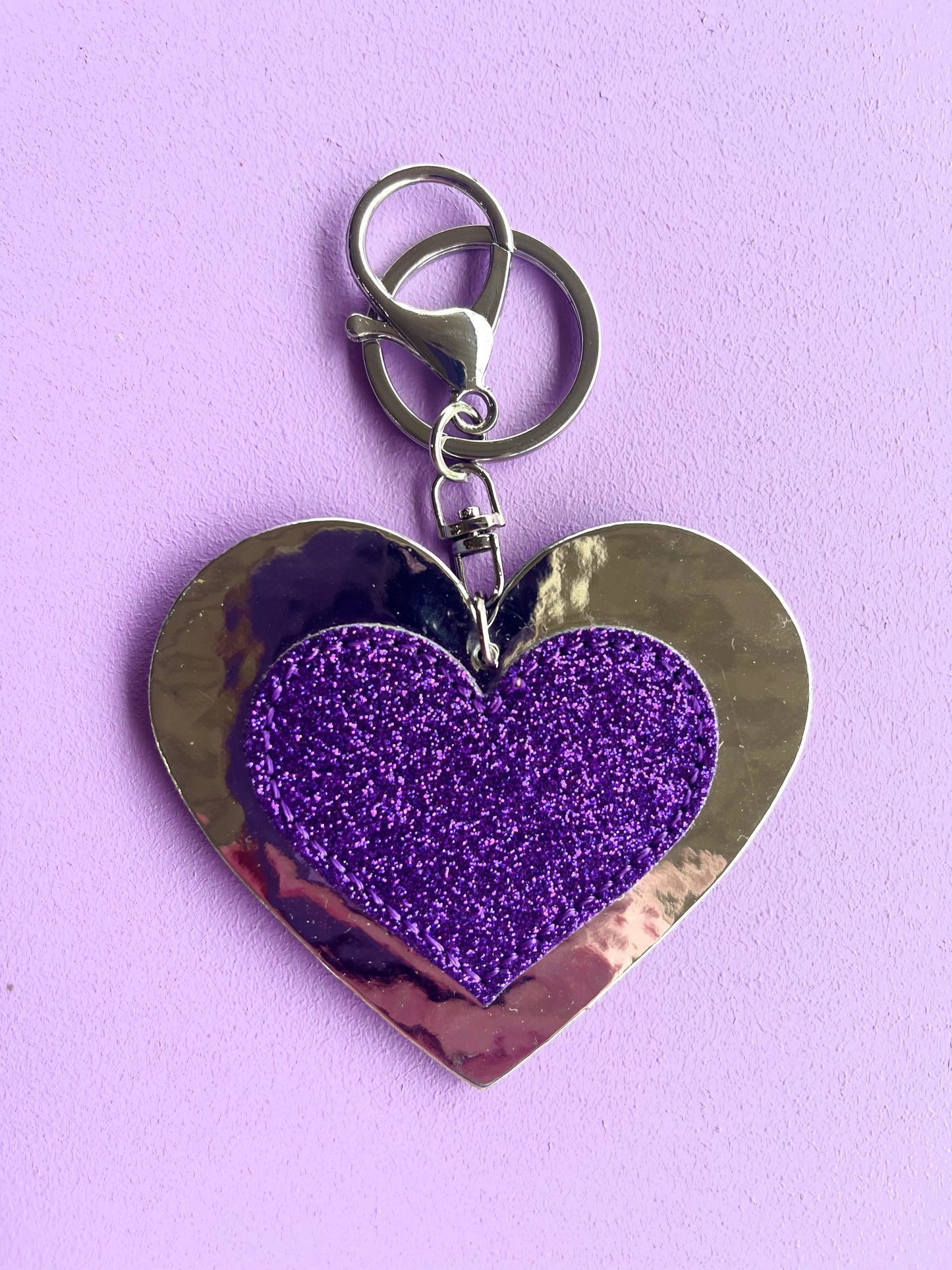 Purple glitter heart keyring accessory for kids. It has a silver metallic background and silver-like clip.